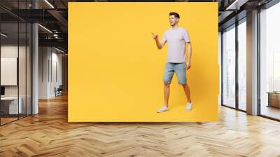 Full body side view young fun happy smiling man he wear light purple t-shirt casual clothes walking go point index finger aside isolated on plain yellow background studio portrait. Lifestyle concept. Wall mural