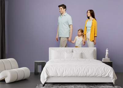 Full body side view young parents mom dad child kid daughter girl 6 years old wearing blue yellow casual clothes hold hands walk go look aside isolated on plain purple background. Family day concept. Wall mural