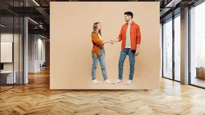 Full body side view young smiling fun couple two friends family man woman wear casual clothes looking to each other shaking hands together isolated on pastel plain light beige color background studio. Wall mural