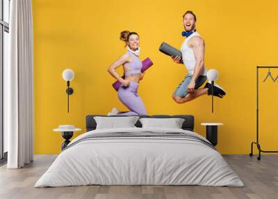 Full body side view young strong fitness trainer sporty two man woman wear blue clothes headphones spend time in home gym jump high hop isolated on plain yellow background. Workout sport fit concept. Wall mural