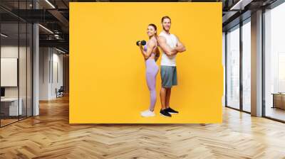 Full body side view young young strong fitness trainer sporty two man woman wear blue clothes spend time in home gym hold in hand dumbbells isolated on plain yellow background. Workout sport concept. Wall mural