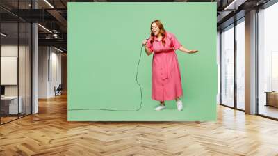 Full body singer caucasian young chubby redhead woman wears casual clothes pink dress sing song in microphone at karaoke club isolated on plain pastel light green color background. Lifesyle concept. Wall mural