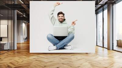 Full body smiling fun happy programmer smart young caucasian IT man wear mint hoody hold use work on laptop pc computer point index finger aside on workspace isolated on plain solid white background. Wall mural