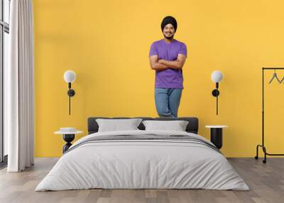 Full body smiling happy fun devotee Sikh Indian man ties his traditional turban dastar wear purple t-shirt hold hands crossed folded look camera isolated on plain yellow background studio portrait. Wall mural