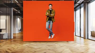 Full body smiling happy young caucasian man wear yellow checkered shirt black t-shirt hold hands crossed folded look camera isolated on plain red orange background studio portrait. Lifestyle concept. Wall mural