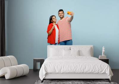 Full body smiling young couple two friends family Indian man woman wear red casual clothes t-shirts together do selfie shot mobile cell phone post photo show v-sign isolated on plain blue background. Wall mural