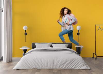 Full body young black teen girl student she wear casual clothes backpack bag jump high look camera run fast hurrying isolated on plain yellow color background. High school university college concept. Wall mural