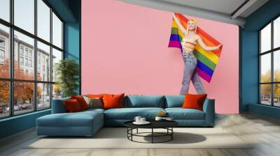 Full body young blond lesbian woman she wear colorful knitted top yellow hat hold striped flag look camera walk isolated on plain pastel light pink background People lgbtq lifestyle fashion concept. Wall mural