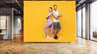 Full body young confident cool strong fitness trainer sporty two man woman wear blue clothes spend time in home gym stand back to back isolated on plain yellow background. Workout sport fit concept. Wall mural