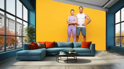 Full body young confident strong fitness trainer sporty two man woman wear blue clothes spend time in home gym stand akimbo look camera isolated on plain yellow background. Workout sport fit concept. Wall mural