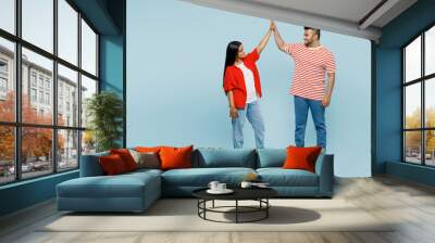 Full body young couple two friend family Indian man woman wear red casual clothes t-shirt together meet together greeting giving high five clapping hand folded isolated on plain blue color background Wall mural