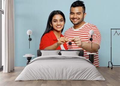 Full body young couple two friends family Indian man woman wear red casual clothes t-shirts together look camera hold in hand apartment keys isolated on pastel plain light blue cyan color background. Wall mural