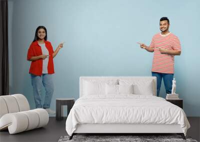 Full body young couple two friends family Indian man woman wear red casual clothes t-shirts together point index fingers on area between them isolated on pastel plain light blue cyan color background. Wall mural