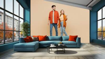 Full body young couple two friends family man woman wear casual clothes together point thumb finger aside indicate on workspace area copy space mock up isolated on pastel plain beige color background. Wall mural