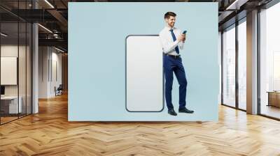 Full body young employee IT business man corporate lawyer in classic formal shirt tie work in office big huge blank screen mobile cell phone with area use smartphone isolated on plain blue background. Wall mural