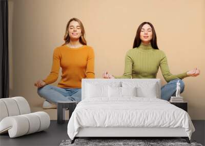 Full body young friends two women wears orange green shirt casual clothes together sit hold spreading hands in yoga om aum gesture relax meditate try to calm down isolated on plain beige background. Wall mural