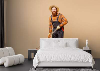 Full body young fun cheerful young bearded man wear straw hat overalls work in garden hold in hand use rake isolated on plain pastel light beige color background studio portrait. Plant caring concept. Wall mural