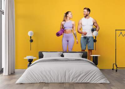 Full body young fun strong fitness trainer sporty two man woman wear blue clothes spend time in home gym hold yoga mat look to each other isolated on plain yellow background Workout sport fit concept Wall mural