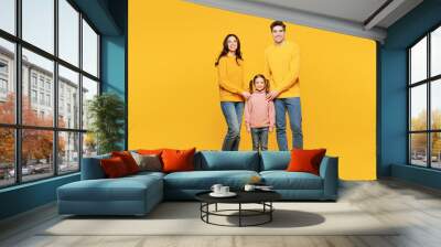 Full body young happy parents mom dad with child kid girl 7-8 years old wear pink sweater casual clothes put hand on little daughter look camera isolated on plain yellow background Family day concept Wall mural