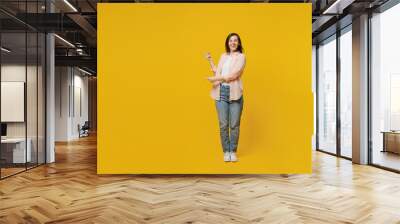 Full body young happy smiling woman she 30s wears striped shirt white t-shirt indicate point index finger aside on workspace area isolated on plain yellow background studio. People lifestyle concept. Wall mural