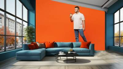 Full body young Indian man he wears white t-shirt casual clothes hold takeaway delivery craft paper brown cup coffee to go isolated on plain orange red background studio portrait. Lifestyle concept. Wall mural