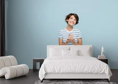 Full body young minded smiling woman wears striped t-shirt casual clothes sitting hold in hand use mobile cell phone isolated on plain pastel light blue background studio portrait. Lifestyle concept. Wall mural