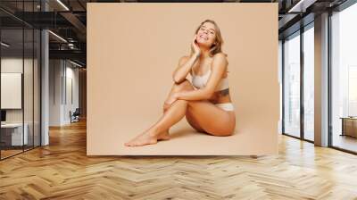 Full body young nice happy lady woman with slim body perfect skin wearing nude top bra lingerie sitting hold face touch herself isolated on plain pastel beige background. Lifestyle diet fit concept. Wall mural