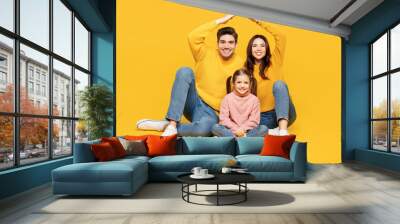 Full body young parents mom dad with child kid girl 7-8 year old wear pink sweater casual clothes hold folded hands above head like house roof isolated on plain yellow background. Family day concept. Wall mural