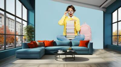 Full body young shocked amazed woman student wear casual clothes sweater backpack bag lower glasses hold stack of many books isolated on plain blue background. High school university college concept. Wall mural