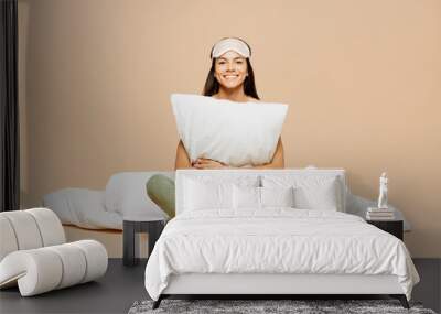 Full body young smiling calm Latin woman wears pyjamas jam sleep eye mask rest relax at home sitting with pillow hold duvet look camera isolated on plain beige background. Good mood night nap concept. Wall mural