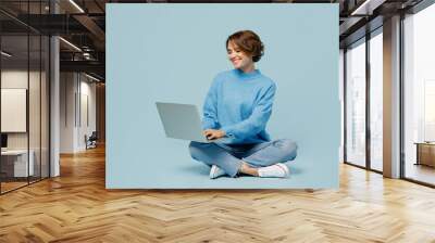 Full body young smiling happy fun cool IT woman wear knitted sweater hold use work on laptop pc computer isolated on plain pastel light blue cyan background studio portrait. People lifestyle concept. Wall mural