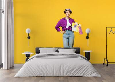 Full body young smiling happy woman wear casual purple shirt do housework tidy up hold basin with laundry clothes look camera isolated on plain yellow background studio portrait. Housekeeping concept. Wall mural