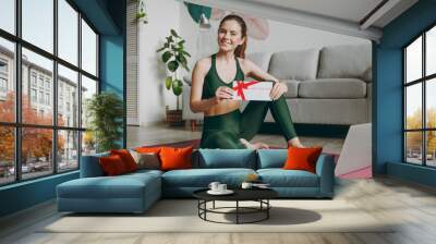 Full body young strong athletic fitness trainer instructor woman wear green tracksuit hold laptop pc computer gift coupon voucher card training do exercises at home gym indoor Workout sport concept. Wall mural