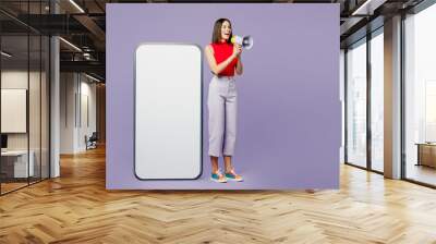 Full body young woman in red tank shirt casual clothes big huge blank screen mobile cell phone smartphone with workspace copy space mockup area scream in megaphone isolated on plain purple background. Wall mural