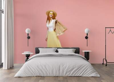 Full length body young happy excited redhead woman in straw hat glasses summer clothes look camera hold package bags with purchases after shopping isolated on pastel pink background studio portrait Wall mural