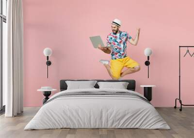 Full length happy traveler tourist man in summer clothes hat jump work on laptop computer doing winner gesture isolated on pink background. Passenger traveling on weekend. Air flight journey concept. Wall mural