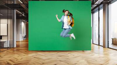 Full length happy young woman student in shirt backpack hold notebooks jumping doing winner gesture isolated on green background studio portrait. Education in high school university college concept. Wall mural