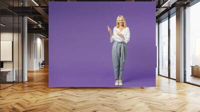 Full length of cheerful funny elderly gray-haired blonde woman lady 40s 50s in white dotted blouse pointing index fingers aside on mock up copy space isolated on violet background studio portrait. Wall mural