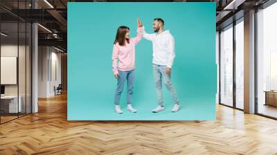 Full length of cheerful young couple two friends man woman in white pink casual hoodie hold hands folded giving high five looking at each other isolated on blue turquoise background studio portrait. Wall mural