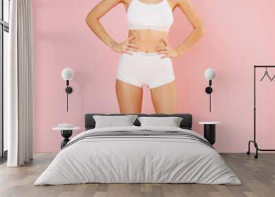 Full length of funny attractive young brunette woman in white underwear showing fit sexy body posing standing with arms akimbo on waist isolated on pastel pink colour background, studio portrait. Wall mural