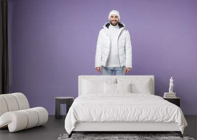 Full length of smiling attractive man in warm white padded windbreaker jacket hat standing looking camera isolated on purple background studio portrait. People lifestyle cold winter season concept. Wall mural