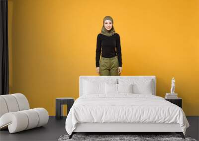 Full length of smiling young arabian muslim woman in hijab black green clothes standing looking camera isolated on bright yellow color background studio portrait. People religious lifestyle concept. Wall mural