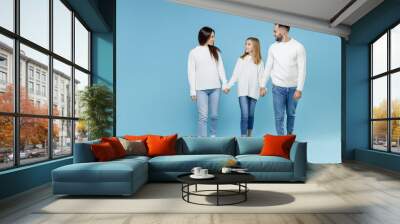 Full length of smiling young parents mom dad with child kid daughter teen girl in white sweaters holding hands walking going isolated on blue background studio portrait. Family day parenthood concept. Wall mural