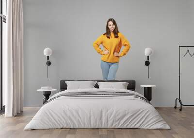 Full length of young smiling caucasian confident cheerful woman 20s wearing knitted yellow casual sweater stand akimbo arms on waist looking camera isolated on grey color background studio portrait Wall mural