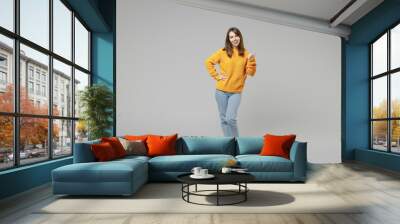 Full length of young smiling positive caucasian happy satisfied woman 20s wearing knitted yellow casual sweater show thumb up gesture looking camera isolated on grey color background studio portrait Wall mural