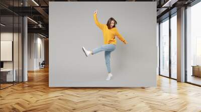 Full length of young smiling relaxed fun positive caucasian happy woman 20s wearing knitted yellow sweater stand raised up leg, outstretched hand isolated on grey color background studio portrait Wall mural