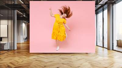 Full length portrait cheerful young redhead plus size body positive female woman girl 20s in yellow dress posing jumping dancing with fluttering hair isolated on pastel pink color background studio. Wall mural