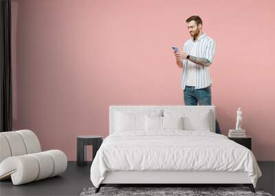 Full length side view young smiling unshaven man 20s in blue striped shirt hold mobile cell phone chat online browsing internet walk isolated on pastel pink background studio. Tattoo translate fun Wall mural