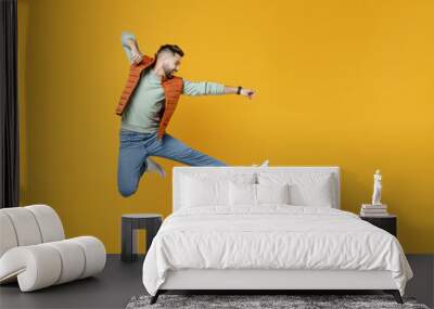 Full length side view young strong powerful fun caucasian man 20s years old wear orange vest mint sweatshirt jump high doing fight gesture clenching fist isolated on yellow background studio portrait Wall mural