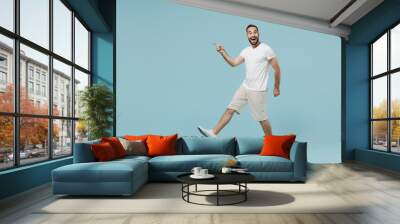 Full length side view young surprised happy man in casual white t-shirt walk going point index finger aside on workspace area copy space mock up isolated on plain pastel light blue background studio Wall mural